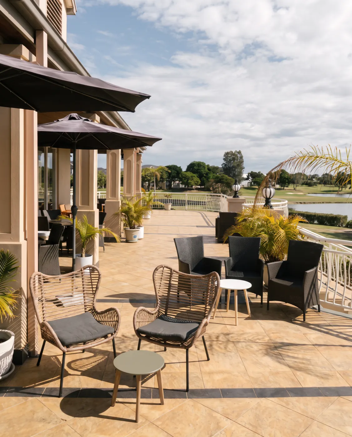 Rattan and charcoal wicker chairs on the clubhouse deck, looking out along the balustrade to the lake and the fairway