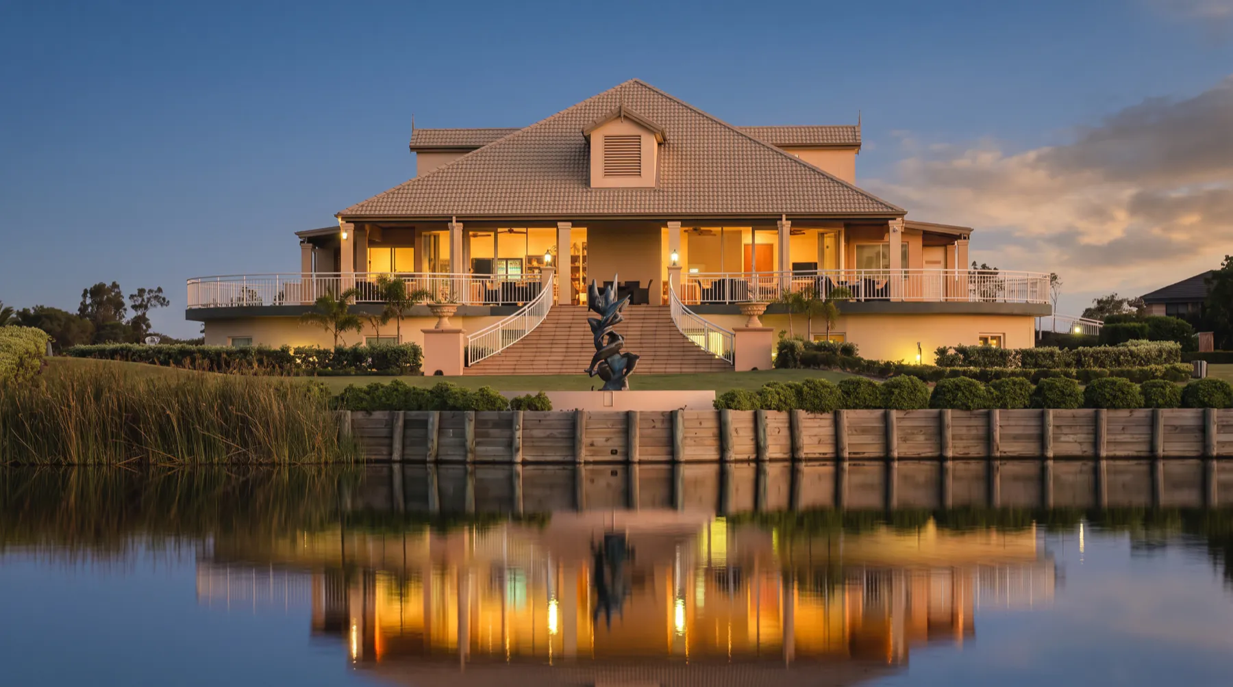 The Harrington Waters clubhouse lit up at dusk, seen across the lake with its reflection on the water