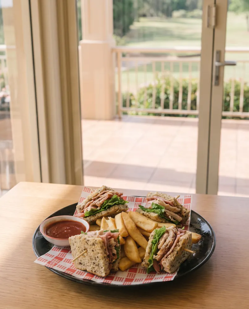 A club sandwich cut into quarters with a mound of thick-cut fries and tomato sauce