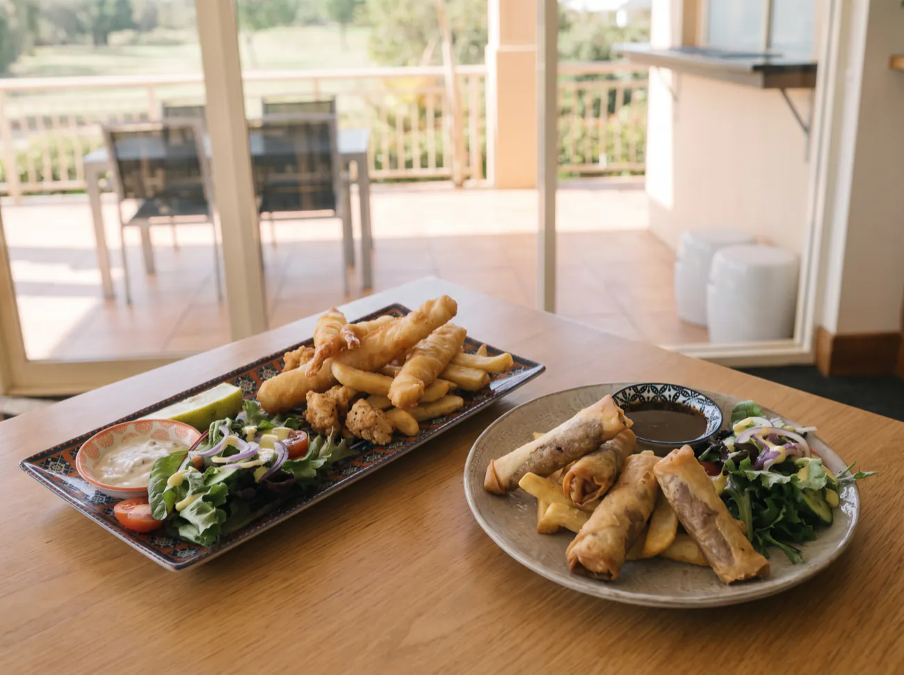 The tempura tasting plate beside the Peking duck spring rolls, both with fries and salad, on a timber table