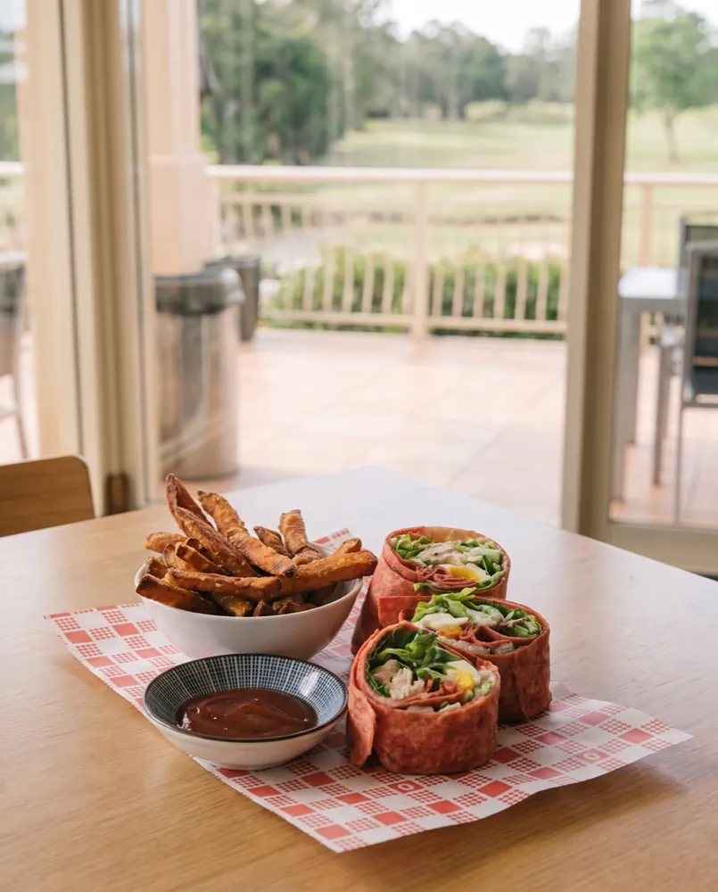 A chicken caesar wrap cut into three, with a bowl of sweet potato fries