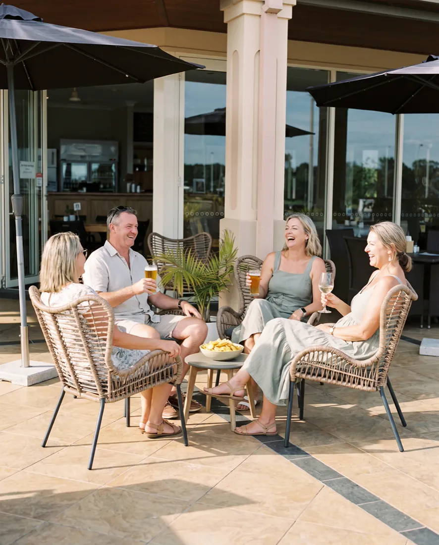 Four friends sitting with beers and wine and a bowl of fries on the clubhouse terrace on a sunny afternoon