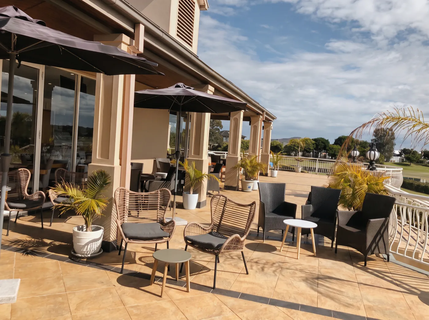 The clubhouse deck looking back along the building, with umbrellas, rattan chairs and the fairway beyond the balustrade