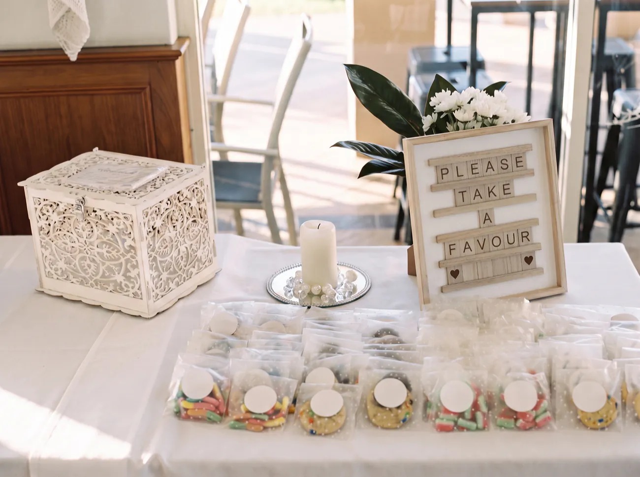 A wedding favour table in the clubhouse, with a white card box, a candle on a mirrored plate and rows of small favour bags